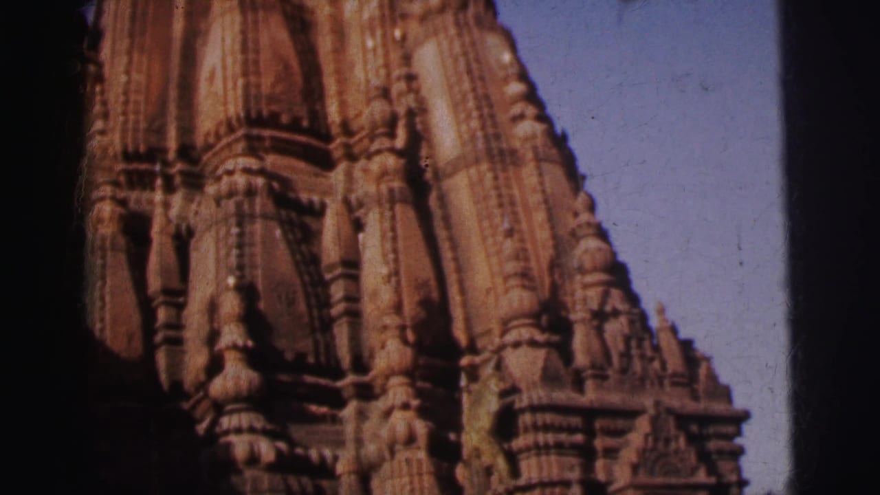 Curvilinear stone temple tower with dense carved ornamentation filling the frame against blue sky.