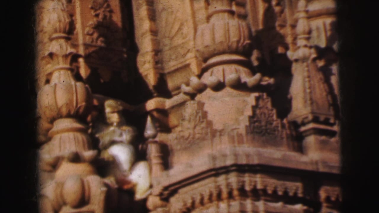 8mm home movie close-up of carved stone temple pillars in Calcutta, India (1962), with a small brown monkey resting on the ornate facade.