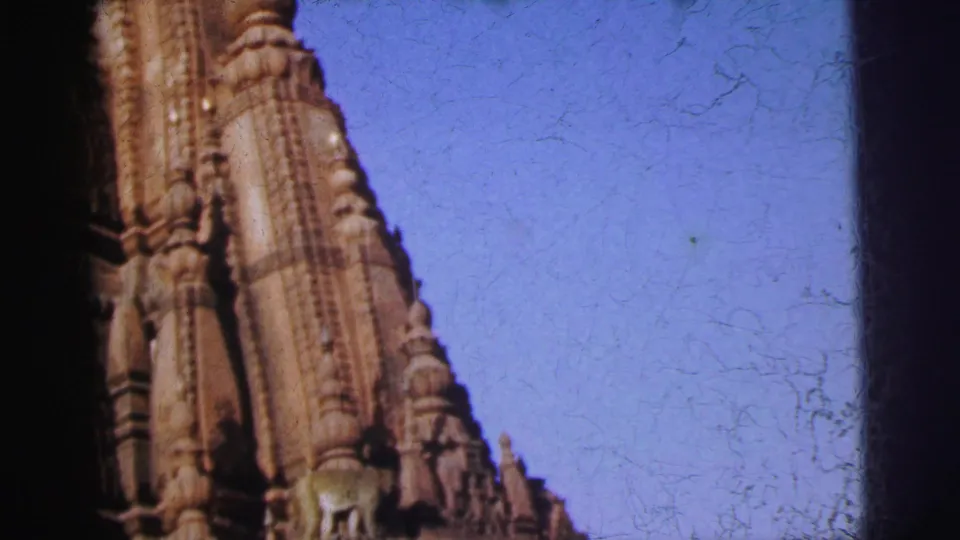 8mm shot of a temple shikhara in Calcutta, India (1962) tapering against open blue sky; film scratches and grain indicate original analog stock.