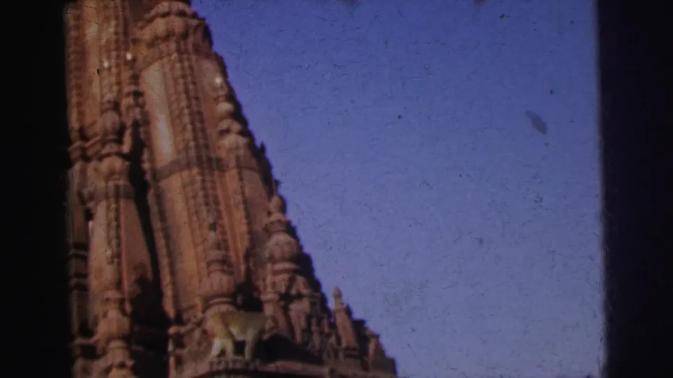 8mm home movie of a temple tower in Calcutta, India (1962), showing tiered carved stonework and small sculpted figures near the base, set against blue sky.