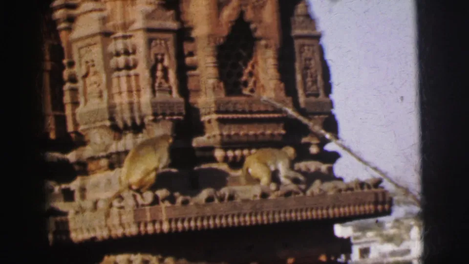 Two or three primates move along a carved stone cornice of an ornate Hindu temple, attributed to Calcutta, India, circa 1962, shot on 8mm film.