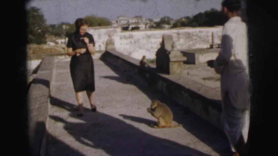 Two figures on an open stone terrace in Calcutta, India, circa 1962 — woman in dark dress and a second person in light clothing — with a monkey between them.