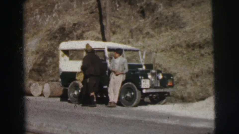 Two men beside an early-series Land Rover on a mountain road, India, circa 1962, 8mm home movie.
