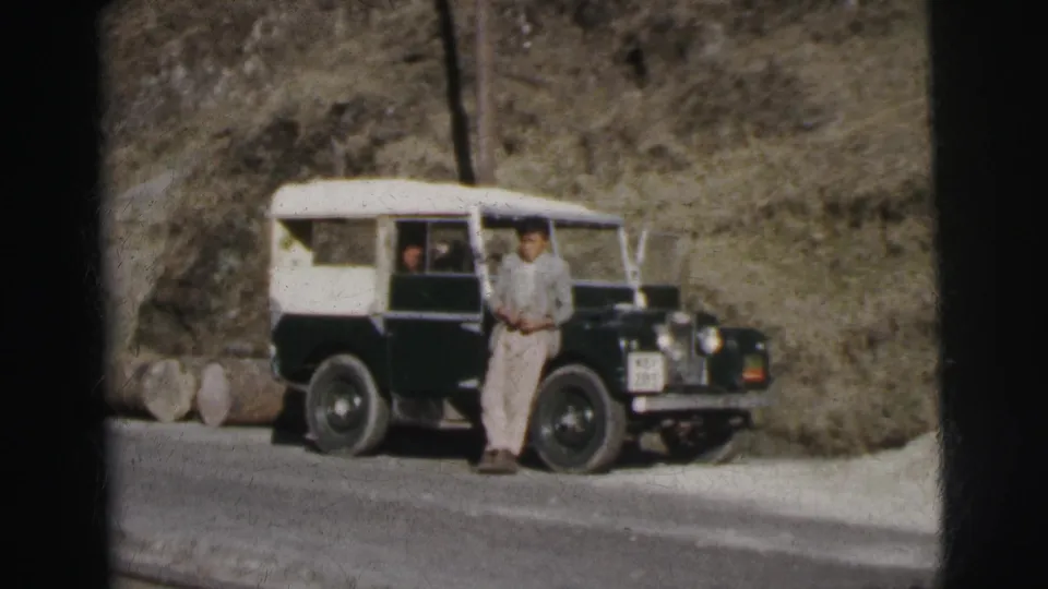 Single man beside an early-series Land Rover on a mountain road, India, circa 1962, 8mm home movie.