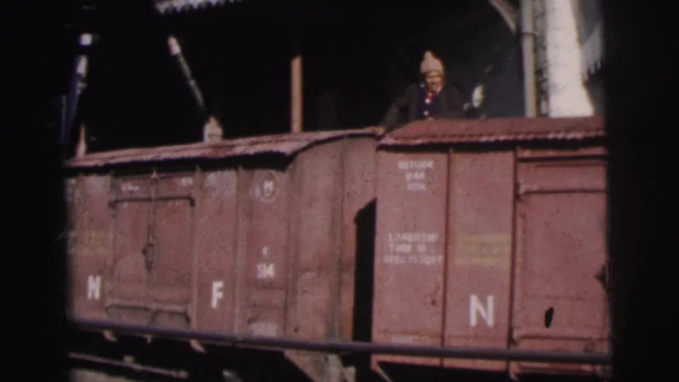 Two figures atop a freight wagon at Calcutta railway yard, c.1962; wagon bears 'NF' marking and capacity text consistent with Indian Railways Northeast Frontier designation.