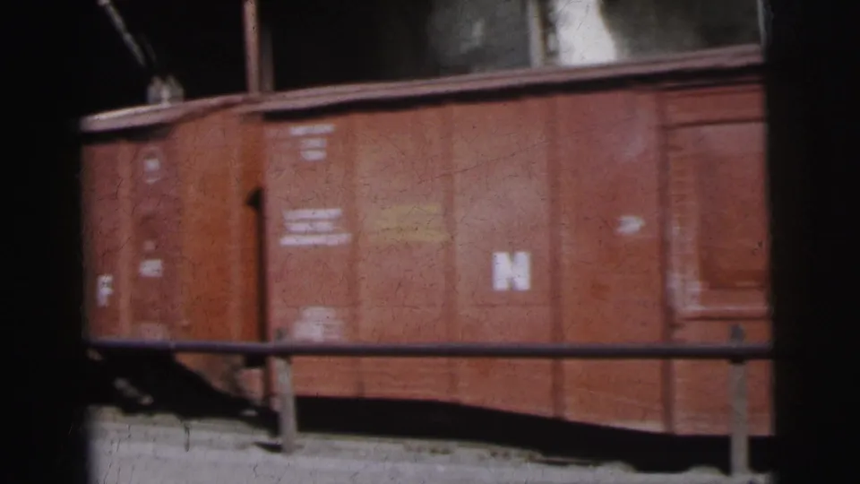 Side panels of a rust-red freight car with white stencilled letter codes including N and F and small painted data text, Calcutta goods yard, circa 1962, 8mm film.