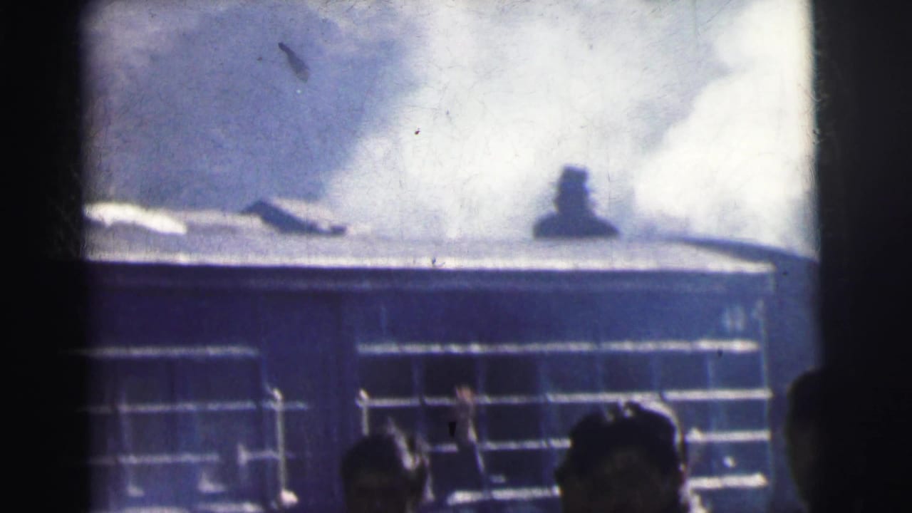 Industrial corrugated building with steam rising above, dark trackside foreground, 8mm home movie frame