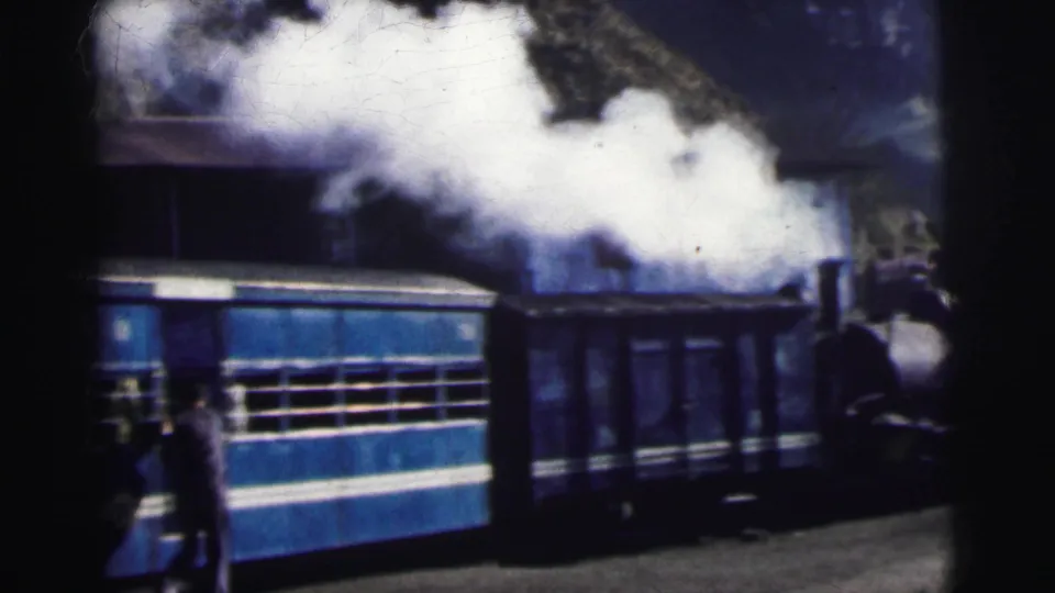 8mm home movie frame, circa 1962 Calcutta, India — blue and white steam passenger train at station platform with thick white smoke rising.