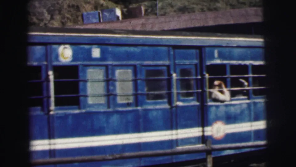 8mm frame, circa 1962 Calcutta — close view of blue and white passenger carriage with a circular railway marking and passenger at open window.