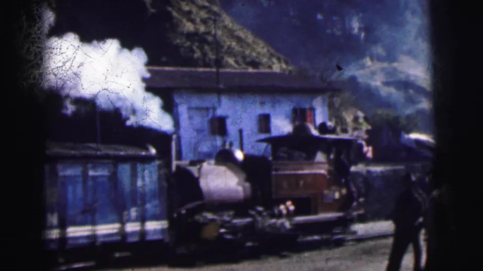 Steam locomotive billowing thick white steam at a mountain railway station with green hills behind, 8mm colour film, India c.1962.