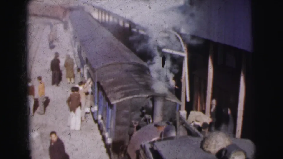Overhead view of passengers alongside blue passenger cars at what appears to be Calcutta railway station circa 1962, captured on 8mm color film.