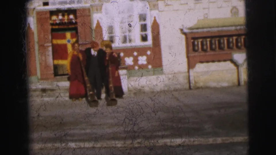 Three figures—two in maroon robes, one in dark coat—at a decorated entrance, Calcutta, 1962; film damage and scratches visible across lower portion of frame.