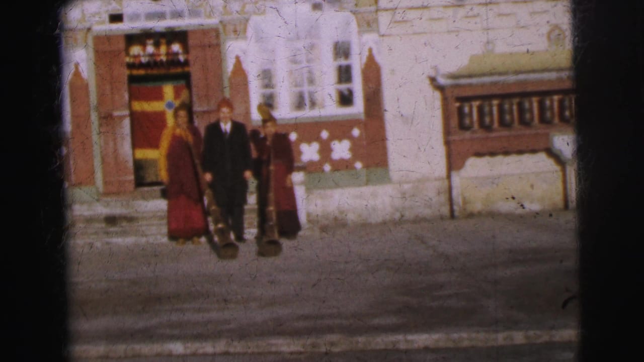 8mm color frame circa 1962 of two figures in red monastic robes and one in a dark suit before an ornate Tibetan-style building, Calcutta, India.