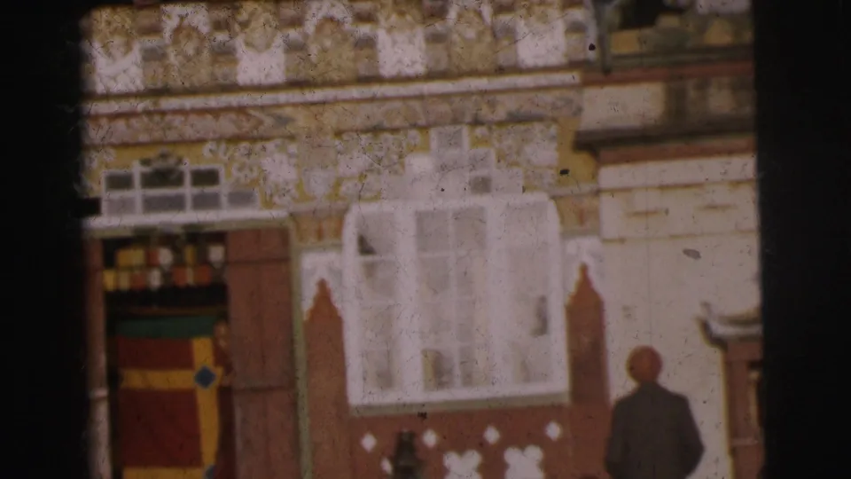 1962 Calcutta, 8mm: decorated facade showing yellow plasterwork with painted motifs, red banding, white arched stucco relief, colorful entrance panels, and an adult figure standing near the building entrance