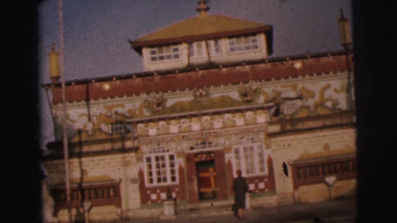 Ornate multi-story building with tiered pagoda-style roof and gilded animal-motif reliefs on a red frieze; a figure stands near the entrance.