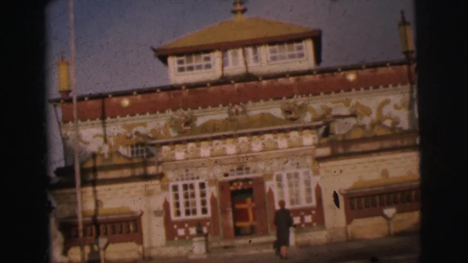 8mm frame from 1962 Calcutta showing an ornate building with pagoda-style tiered roof, gold relief carvings on a red frieze band, and a lone figure near the entrance.