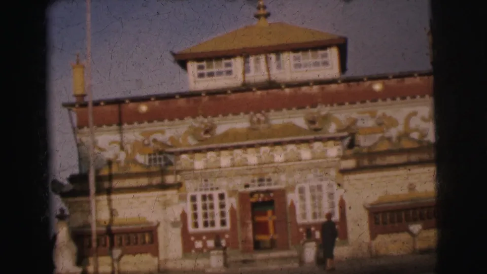 8mm frame from 1962 Calcutta; ornate building with tiered pagoda roof and gilded relief frieze, with a figure visible to the right of the entrance.