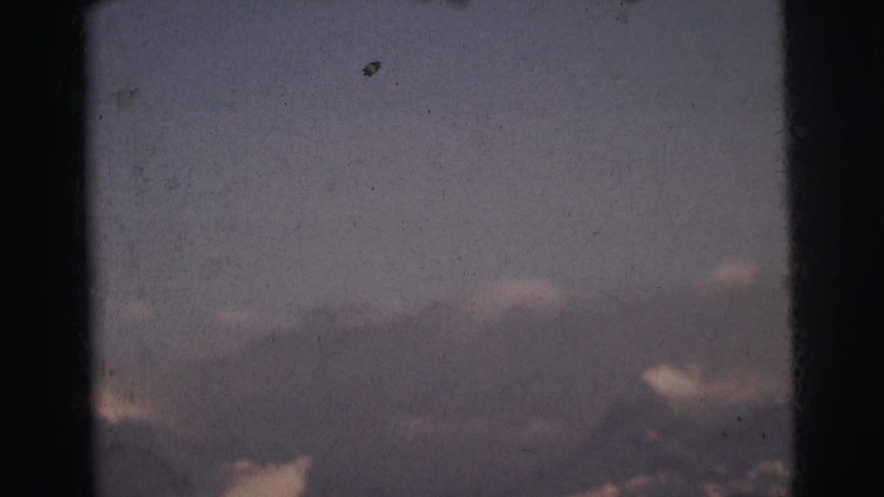 8mm film frame c. 1962 showing a dark mountain ridge silhouette below a blue-grey cloud-filled twilight sky, India.