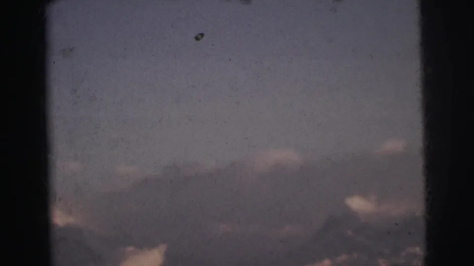 8mm film frame c. 1962 showing a dark mountain ridge silhouette below a blue-grey cloud-filled twilight sky, India.