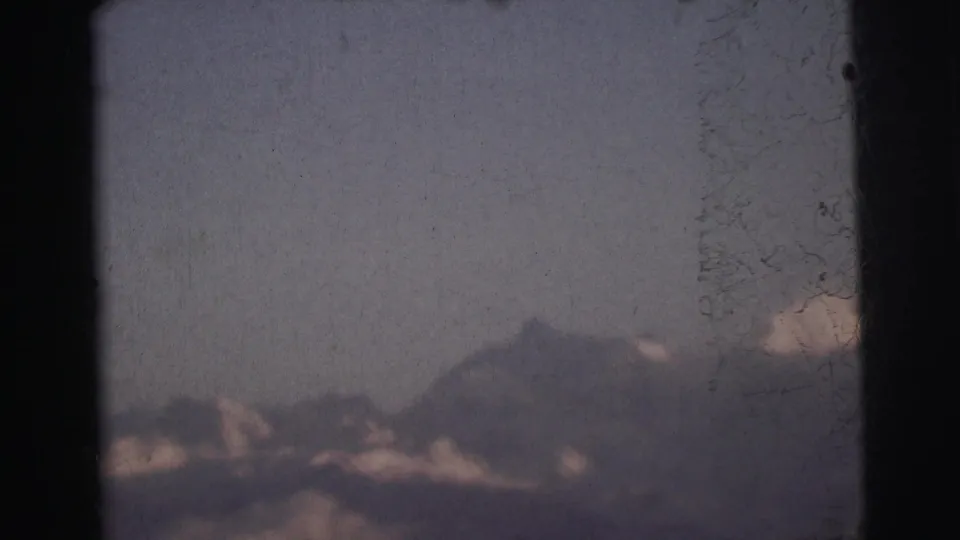 Distant mountain peak against overcast sky in 8mm home movie footage from India circa 1962, with film scratches and heavy grain visible.