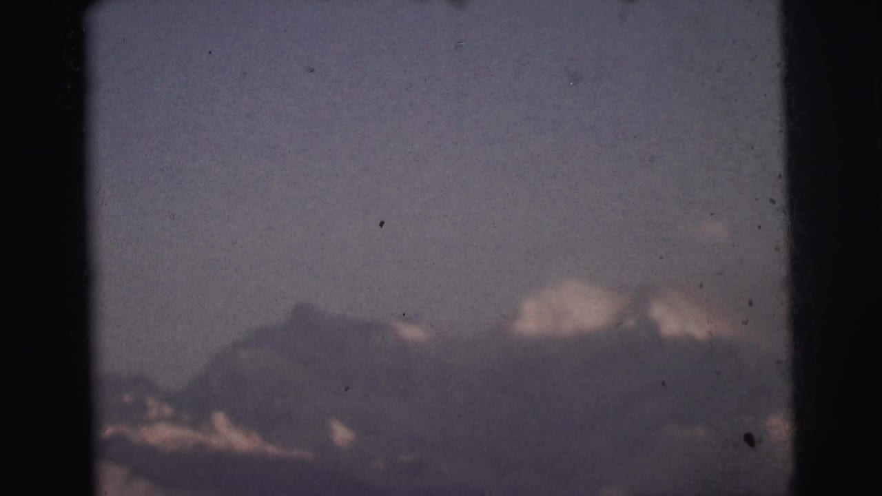 Mountain summit emerging from cloud cover, 8mm film frame with dark border vignette and visible grain.