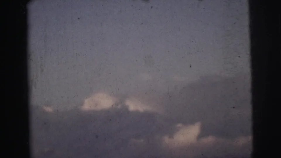 Cloud-dominated frame with mountain ridgeline barely visible at lower edge, 8mm home movie footage from India circa 1962.