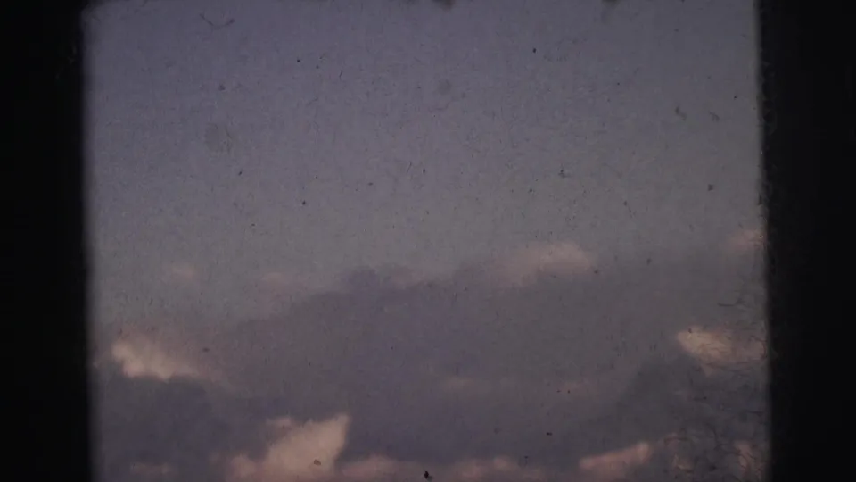 Final frame showing diffuse clouds and haze above a low ridgeline, 8mm home movie footage from India circa 1962, with prominent grain.