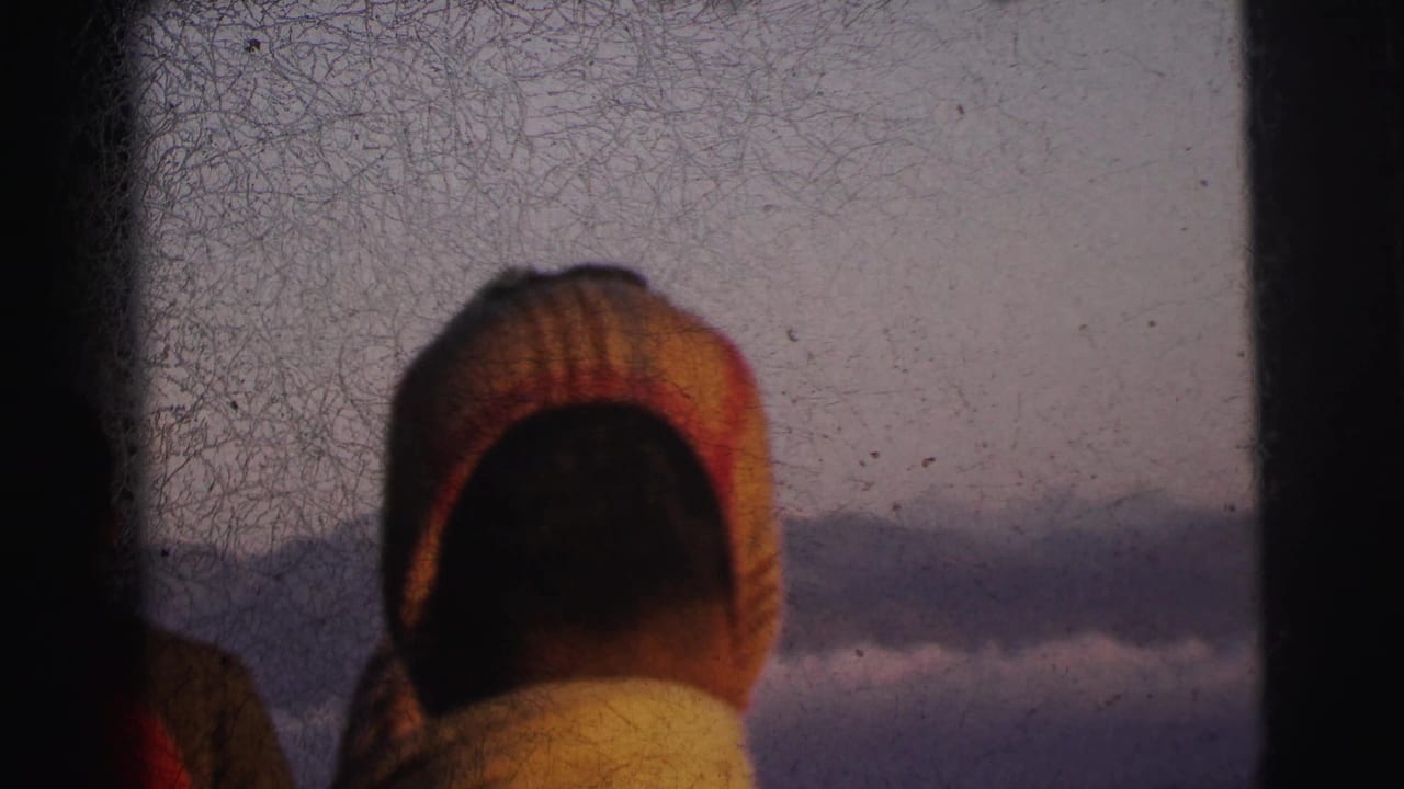 Rear view of passenger in striped knitted cap looking out a train window at hazy mountains, 8mm film, circa 1962.