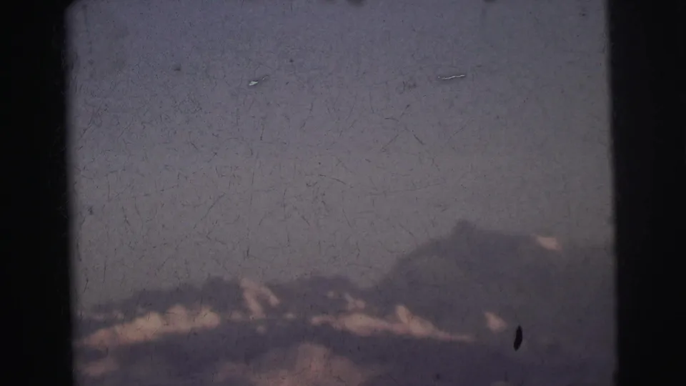 Unobstructed view of snow-capped mountains under a pale overcast sky through a train window, 8mm home movie, India, 1962.