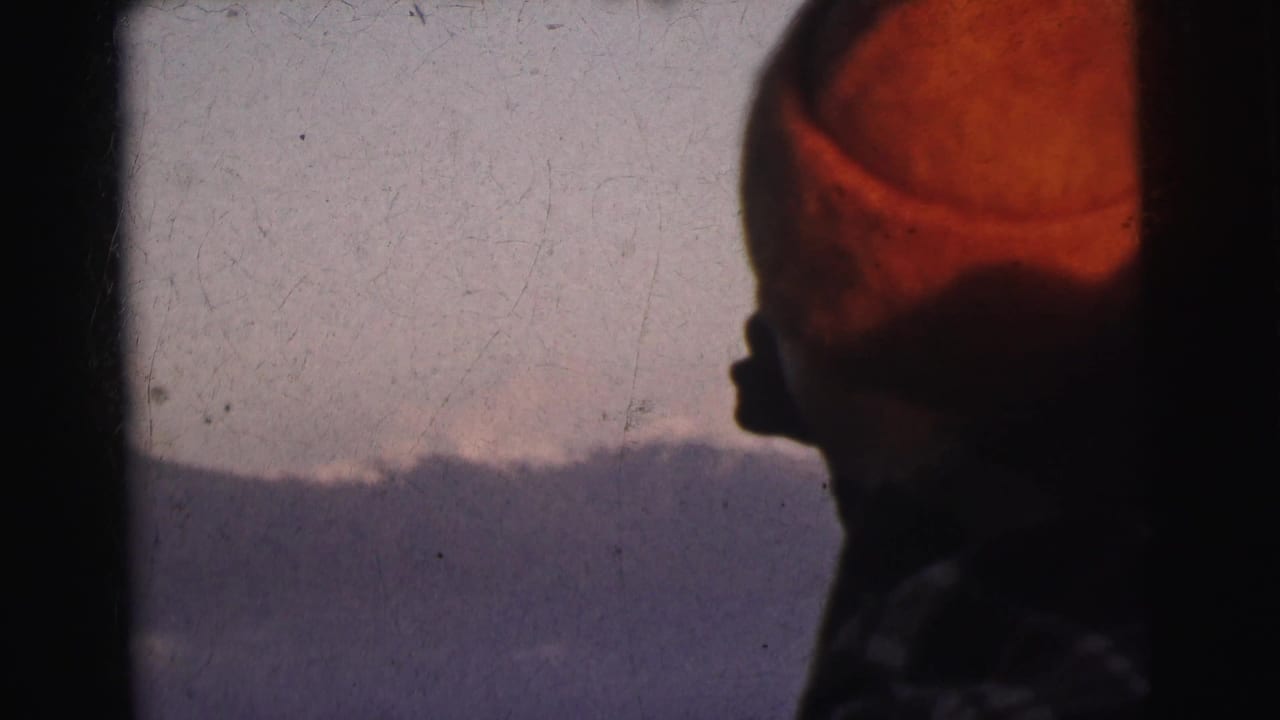 Close profile view of a figure in an orange-red knit hat facing a distant mountain ridge, 8mm home movie, India, circa 1962.