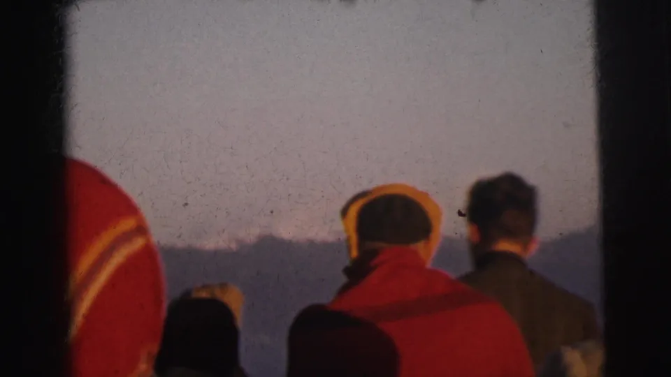 Small group in cold-weather jackets and hats seen from behind, watching a mountain horizon, 8mm home movie, India, circa 1962.