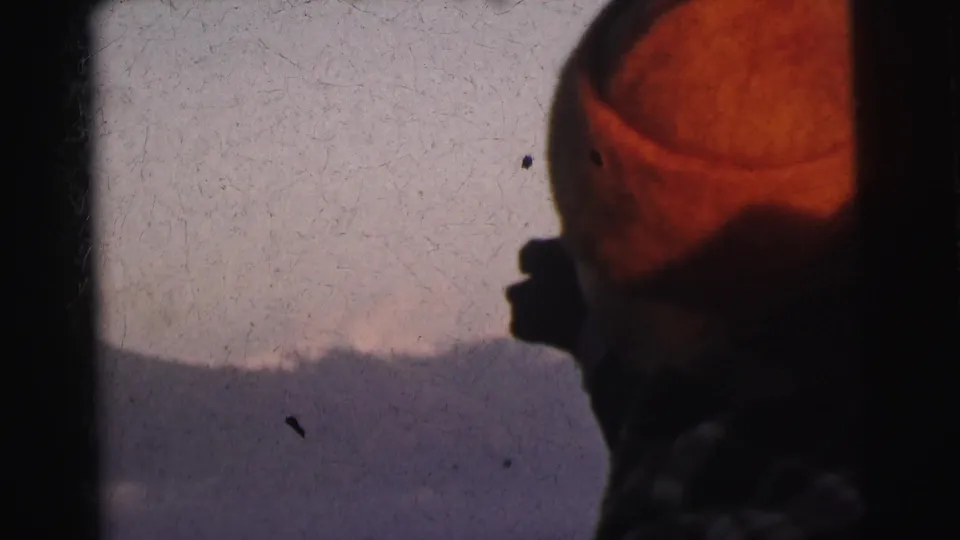 Side profile of a man wearing a red knit beanie against a pale sky and distant mountain silhouette, 1962 8mm home movie footage from India.