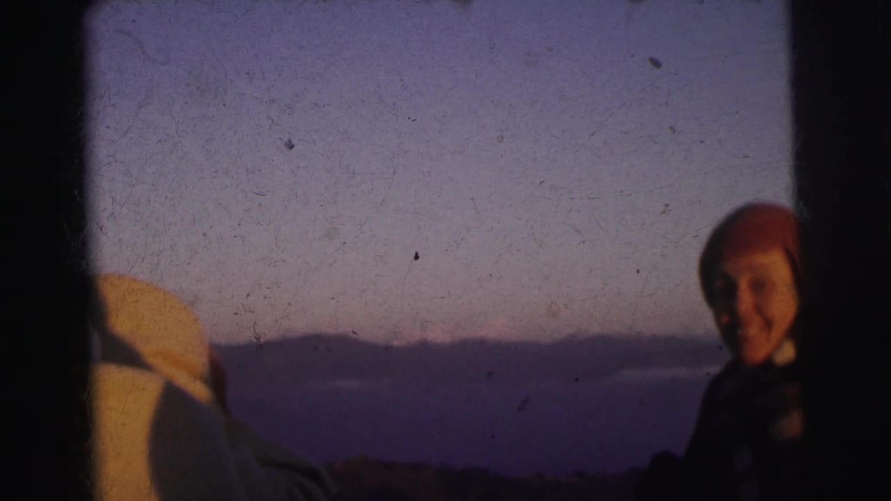 Smiling figure in a red knit beanie at what appears to be a high-altitude viewpoint, circa 1962; 8mm film with characteristic grain and edge vignetting.