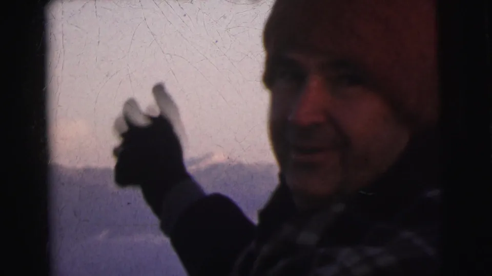 Man pointing with a gloved hand toward snow-capped mountains at what appears to be a high-altitude location, circa 1962; heavy film grain and surface scratches visible.