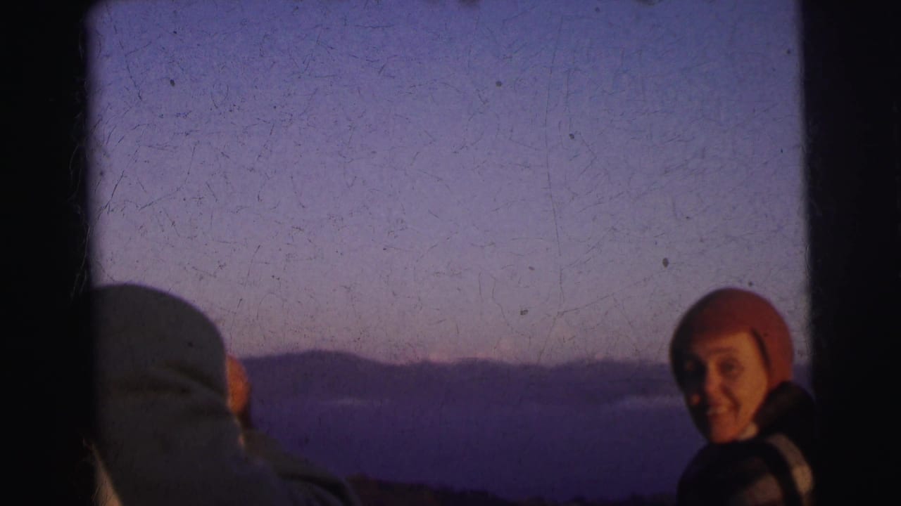 Smiling adult in red wool beanie at twilight, second adult seen from behind at left; 8mm footage described as Calcutta, India, 1962.