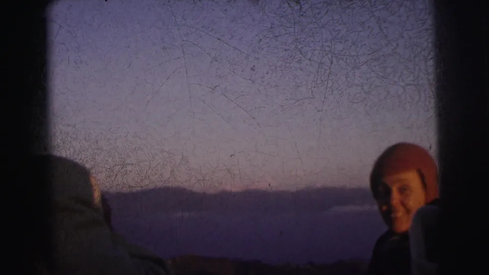 Closing frame: smiling adult in red beanie at dusk, second figure in pale wrap at lower left; 8mm footage described as Calcutta, India, 1962.