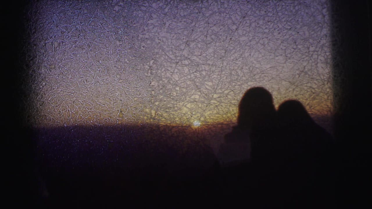 Two adult silhouettes at what metadata identifies as a high vantage point in Calcutta, 1962, watching a sunset; extreme emulsion crazing dominates the upper frame.