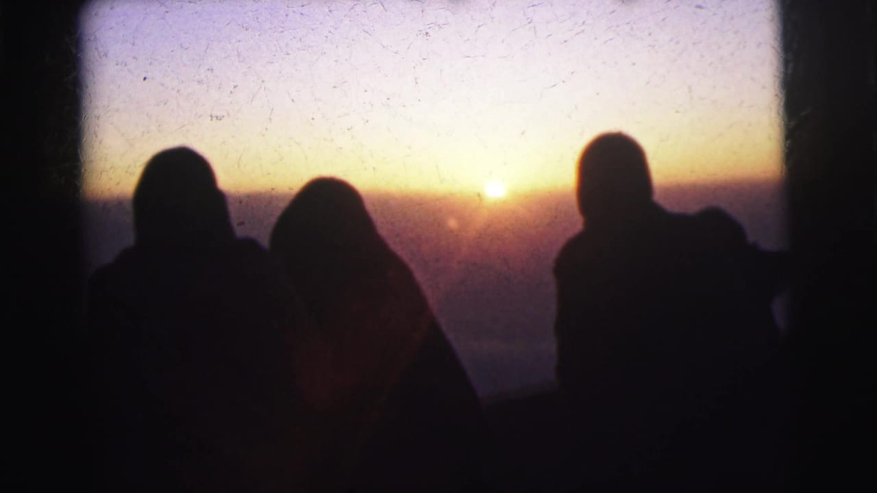 Three adult silhouettes overlook a glowing golden horizon at what metadata places as Calcutta, 1962; warm orange sky with visible sun disk, film grain, and one figure appearing to wear a head covering.