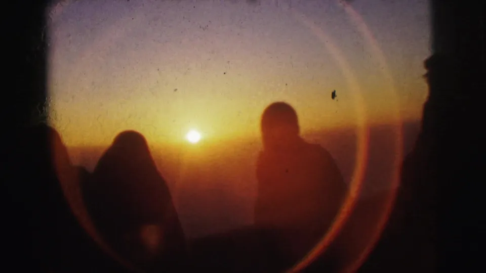 Two adult silhouettes against a bright golden sunset; a circular lens flare, a common artifact in direct-sun 8mm shooting, fills the right portion of the frame; metadata places this in Calcutta, 1962.