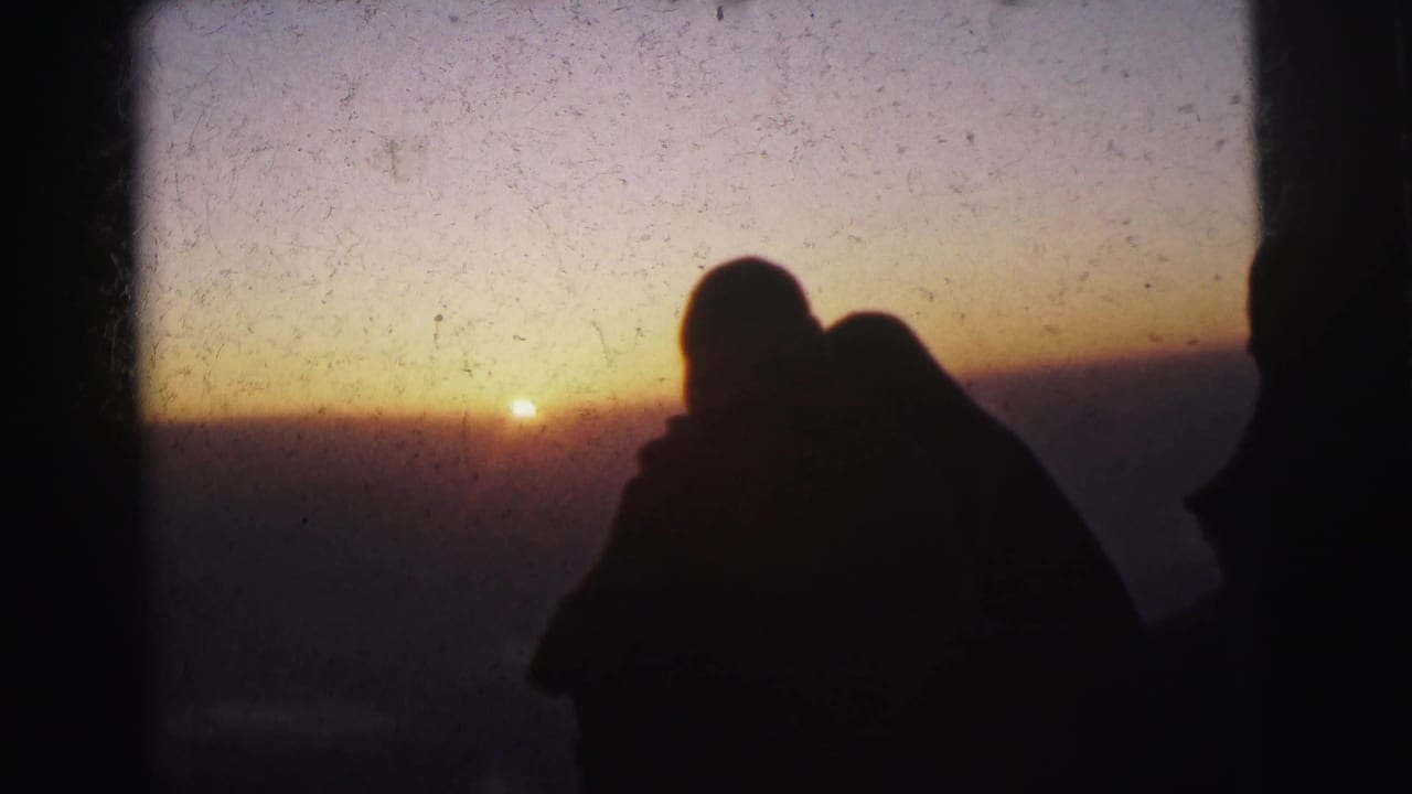 Two dark figures embrace in silhouette as the sun nears the horizon.