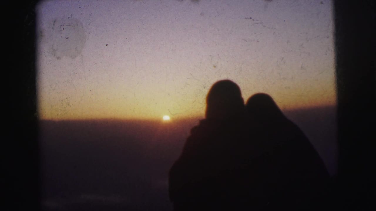 Silhouetted couple framed below a glowing sunset sky with visible film texture.