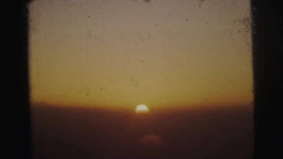 Flat-horizon sunset with the sun at the horizon line and a warm orange sky gradient, 8mm home movie footage possibly from the Calcutta region, circa 1962.