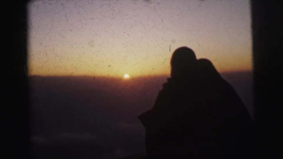 Silhouettes of two people in close proximity watching a flat-horizon sunset, faces unidentifiable, 8mm home movie footage from Calcutta, India, circa 1962.