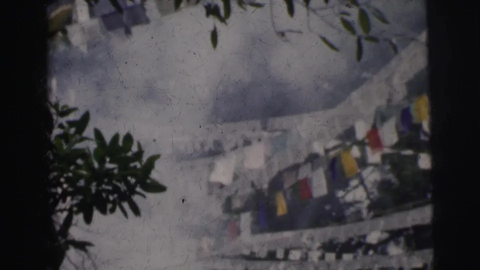 8mm frame circa 1962 Calcutta; lower framing reveals pennant flags in red, yellow, and blue more prominently, with tree branches at the edges.