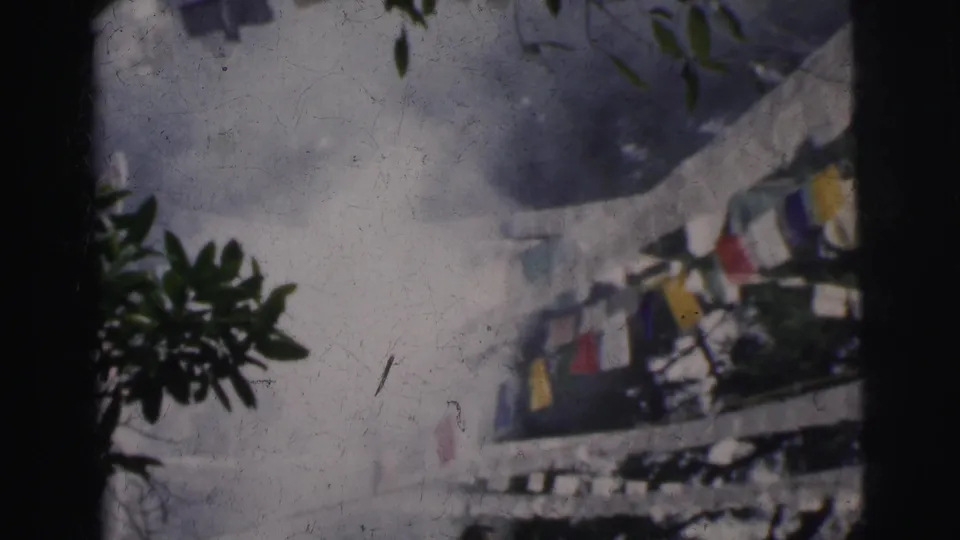 Final 8mm frame circa 1962 Calcutta; flags in primary colors remain the focal point with leafy foliage at the edges and the white building structure visible behind.