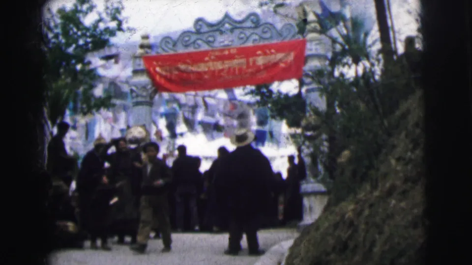 8mm color film frame of a crowd under a red banner at a decorated archway gate, Calcutta, India, circa 1962; people visible from behind.