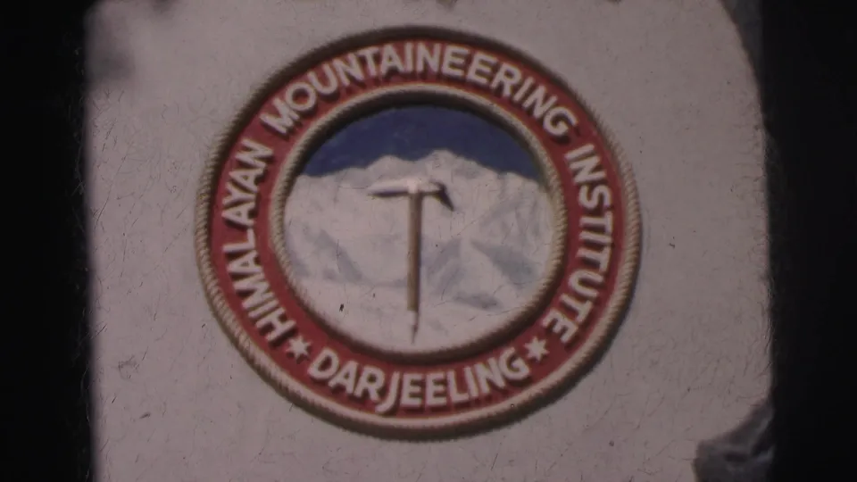 1962 8mm close-up of the Himalayan Mountaineering Institute Darjeeling emblem with mountain and ice axe design.