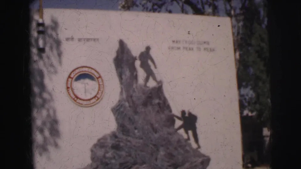 Wide 8mm view of the HMI climbing monument display, with figures ascending rock forms and visible peak-to-peak motto text.