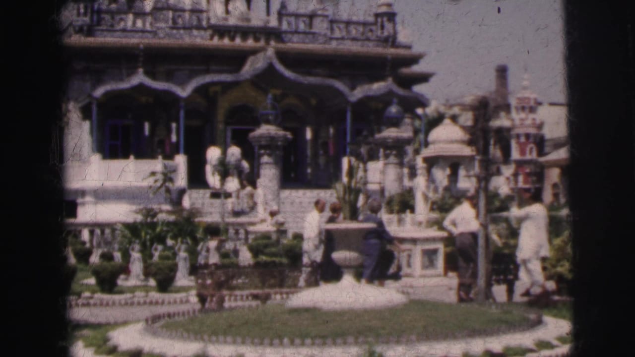 1962 8mm frame of tourists in India visiting a landscaped complex with carved arches, domed details, and white statues.