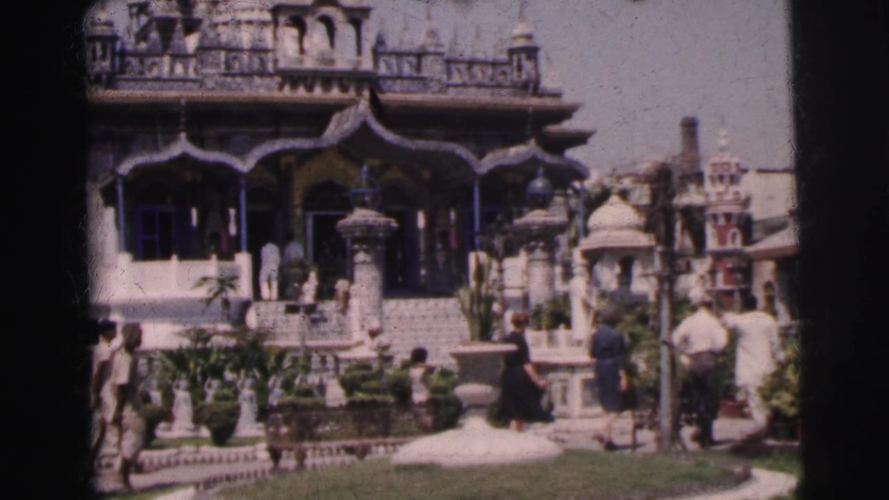 Tourists in 1962 India move through a sunny garden courtyard before an elaborately decorated landmark facade.